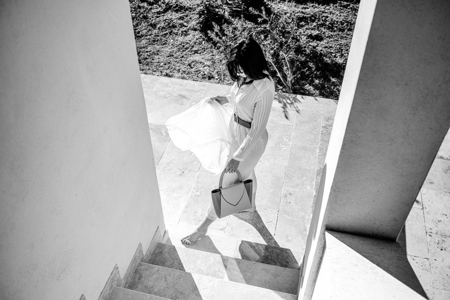 Femme élégante descendant des escaliers pieds nus avec le sac Désinvolte à la main, prise de vue en noir et blanc.