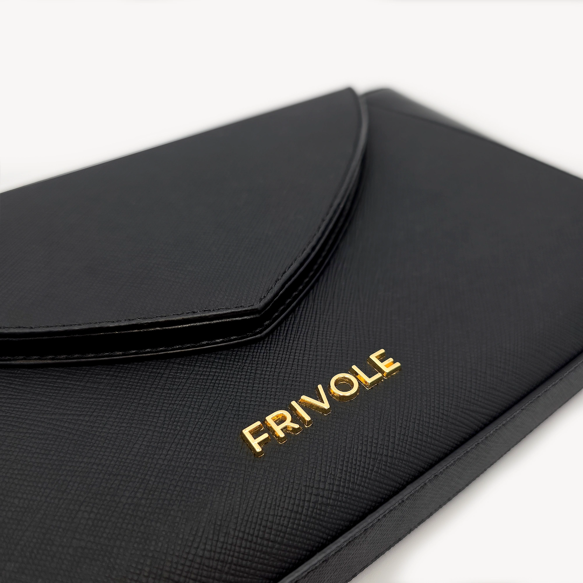 Détail du logo doré Frivole sur le sac un Brin Désinvolte noir, texture grainée.