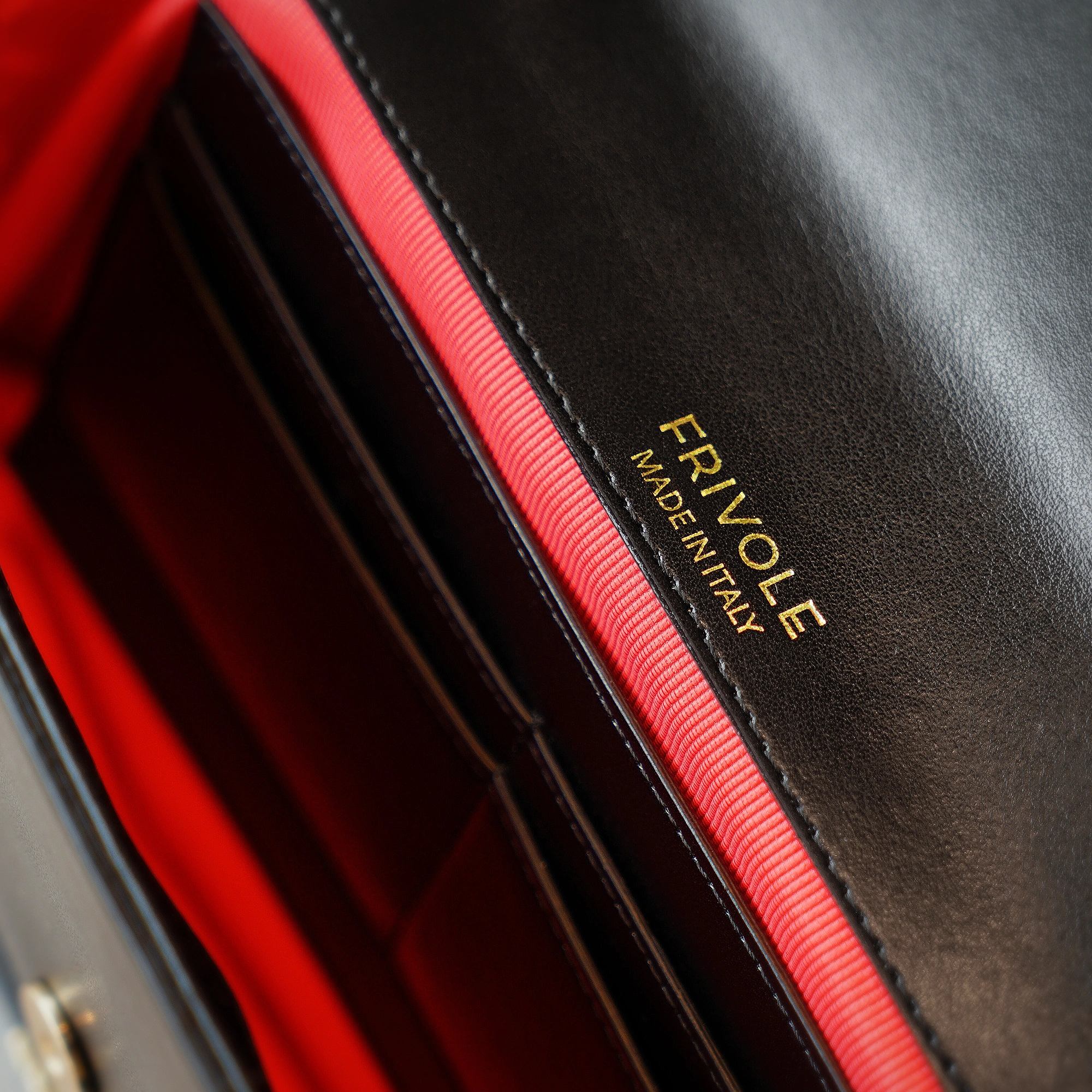 Intérieur du sac un brin désinvolte noir, doublure rouge, logo doré Made in Italy.