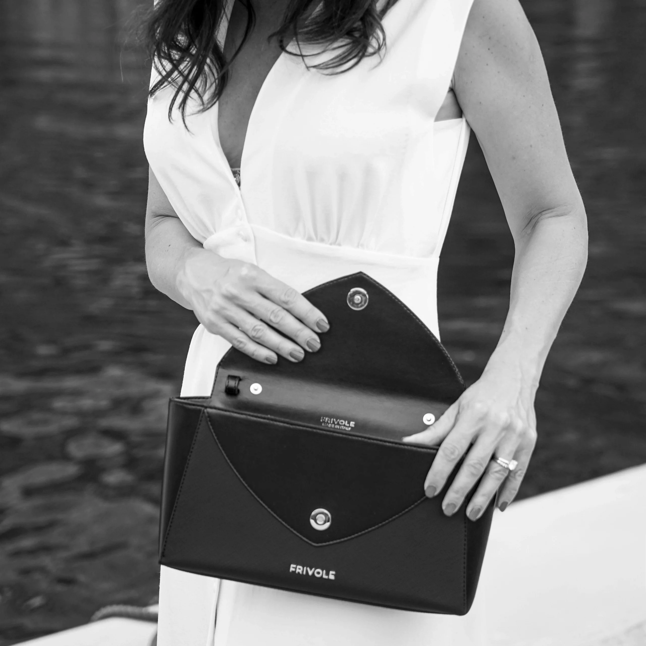 Femme en robe blanche tenant la pochette noire Un Brin Désinvolte de Frivole ouverte, en bord de mer.